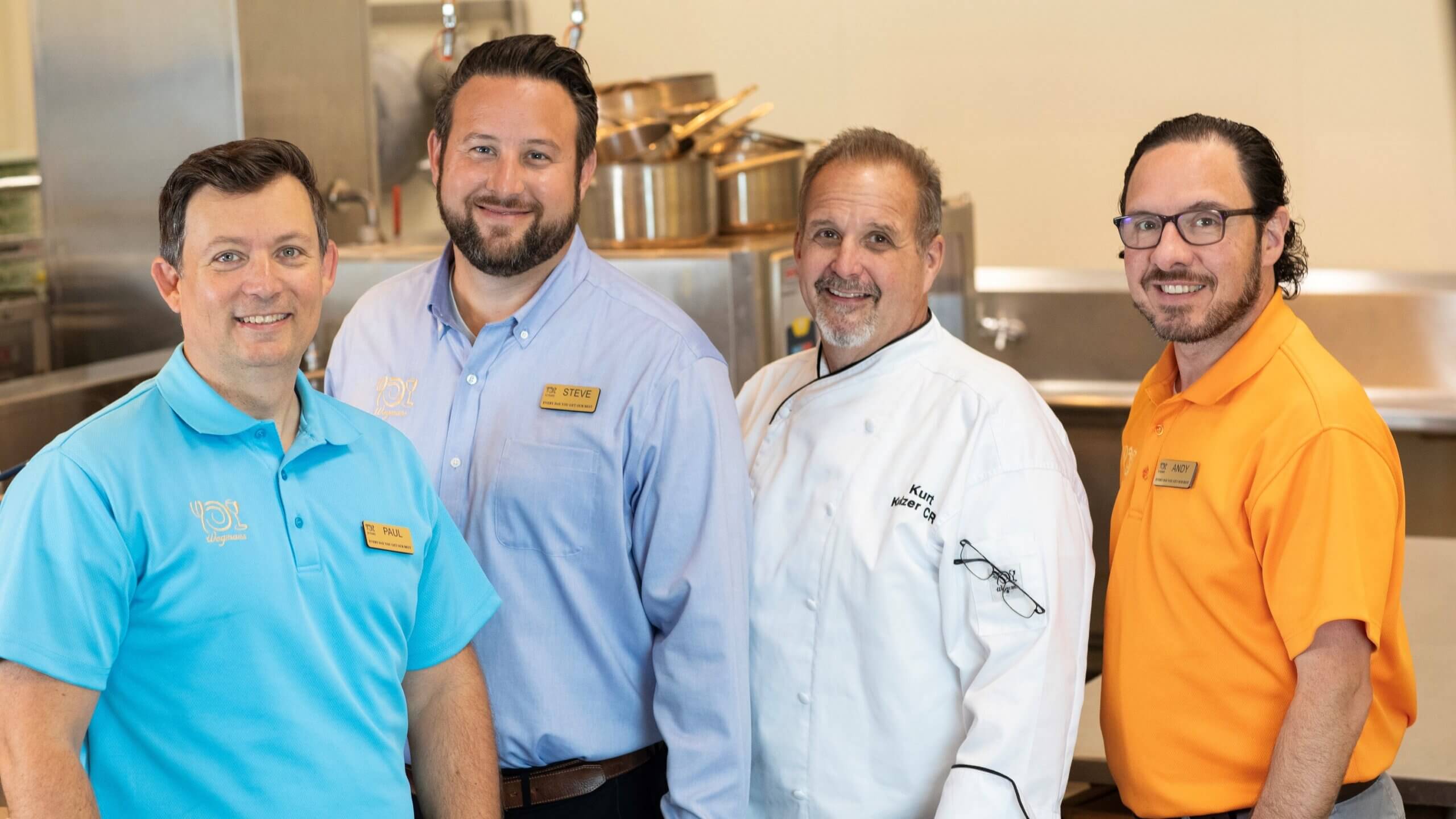 Paul, Steve, Kurt, and Andy standing together smiling in test kitchen wearing Wegmans polos