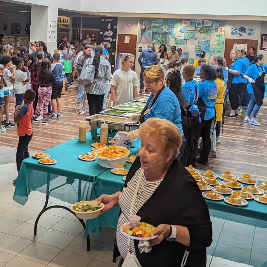Community members in line for plant-forward meal being served by school staff.